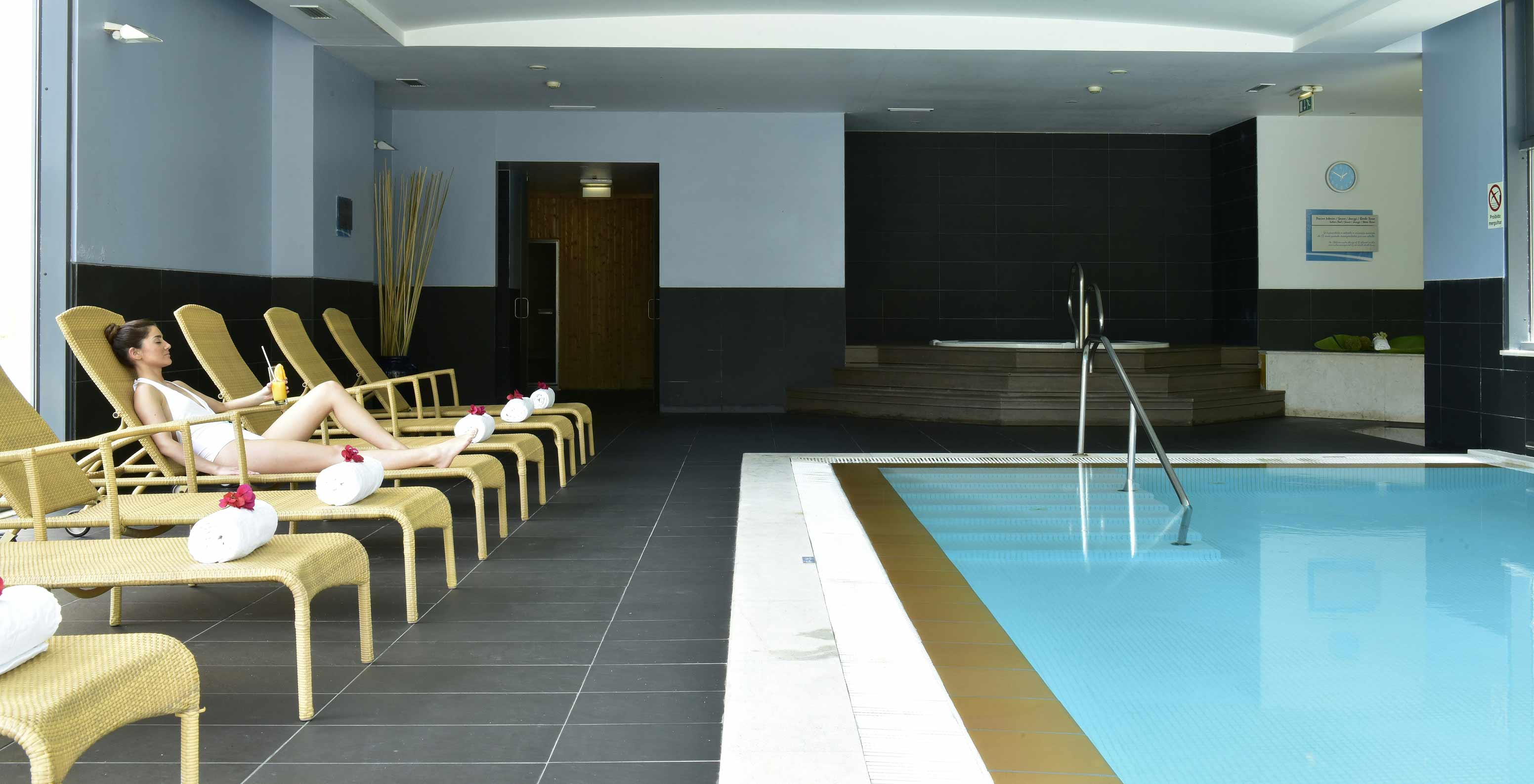 Hóspede a relaxar nas espreguiçadeiras da piscina interior no Pestana Alvor Park, Aparthotel 4 Estrelas no Alvor com Piscina