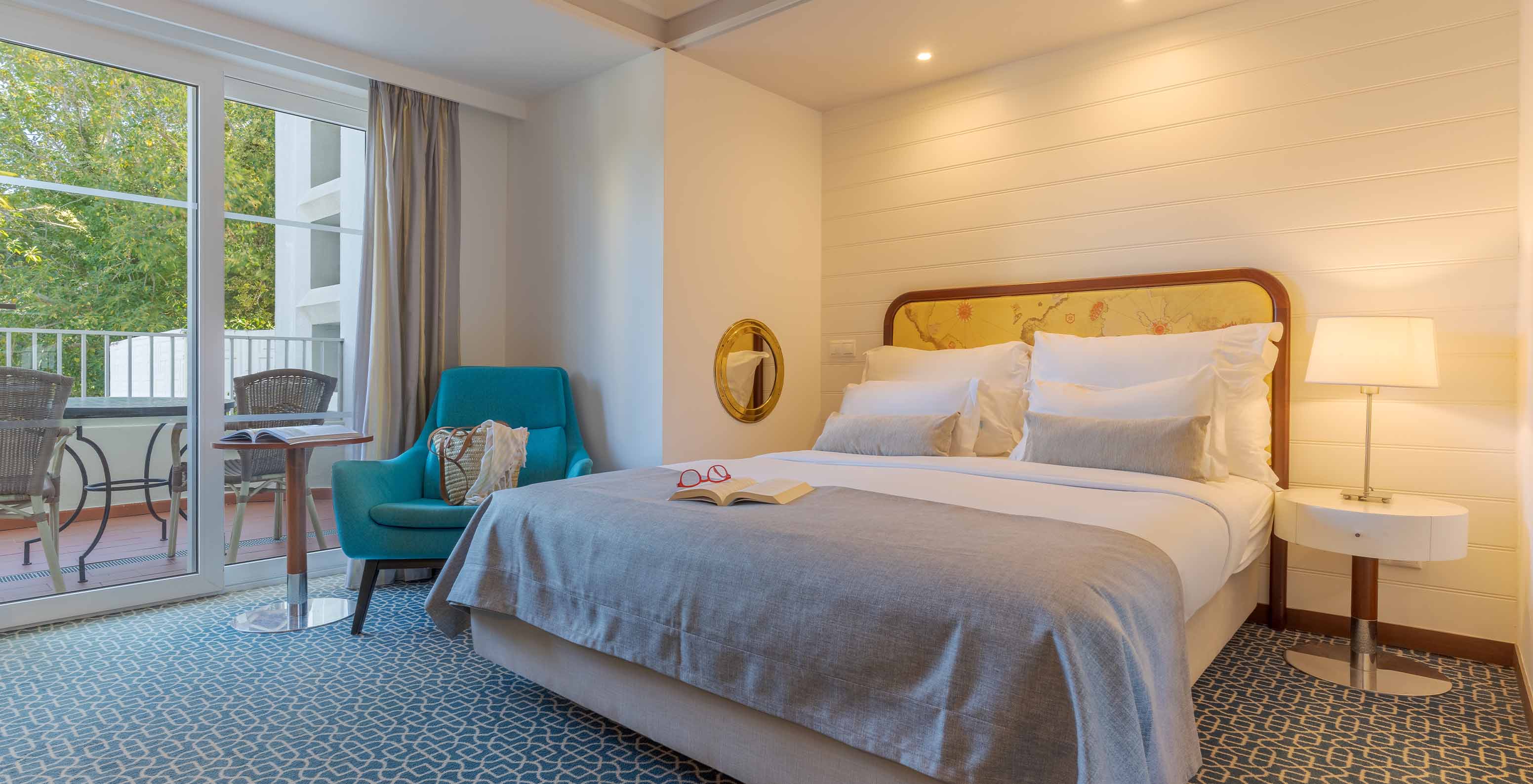 O Deluxe Vista Jardim do Pestana Alvor Praia tem uma cama de casal, cadeirão azul e janela para a varanda com cadeiras e mesa