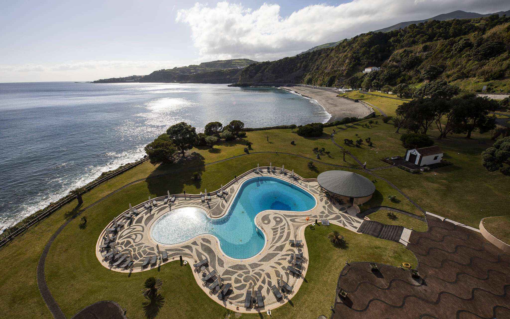 Piscina com vista para o mar e praia junto ao Pestana Bahia Praia em São Miguel num dia parcialmente nublado