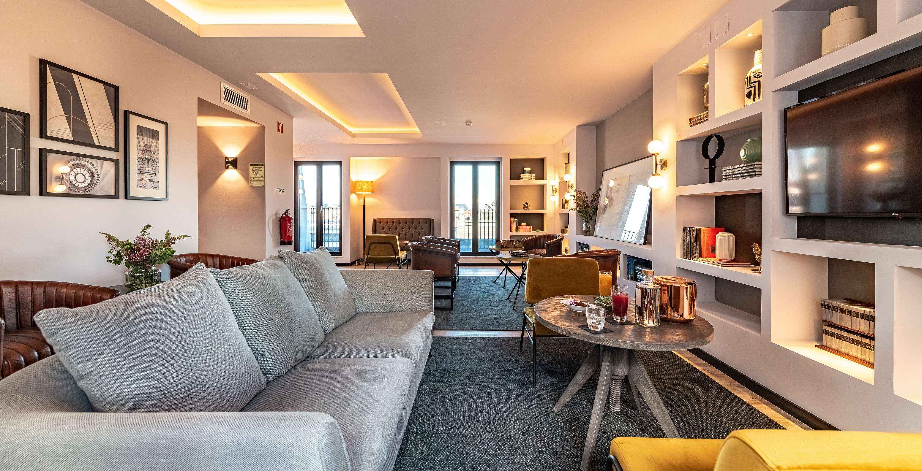 Lounge com sofás, cadeiras, mesas, quadros, televisão, tapetes e objetos de decoração com janelas com vista para a cidade