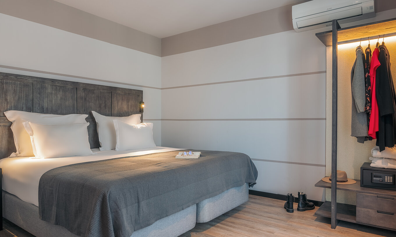 A Rooftop Junior Suite do Pestana Lisboa Vintage tem uma cama de casal, umas botas no chão de madeira e um armário com roupa