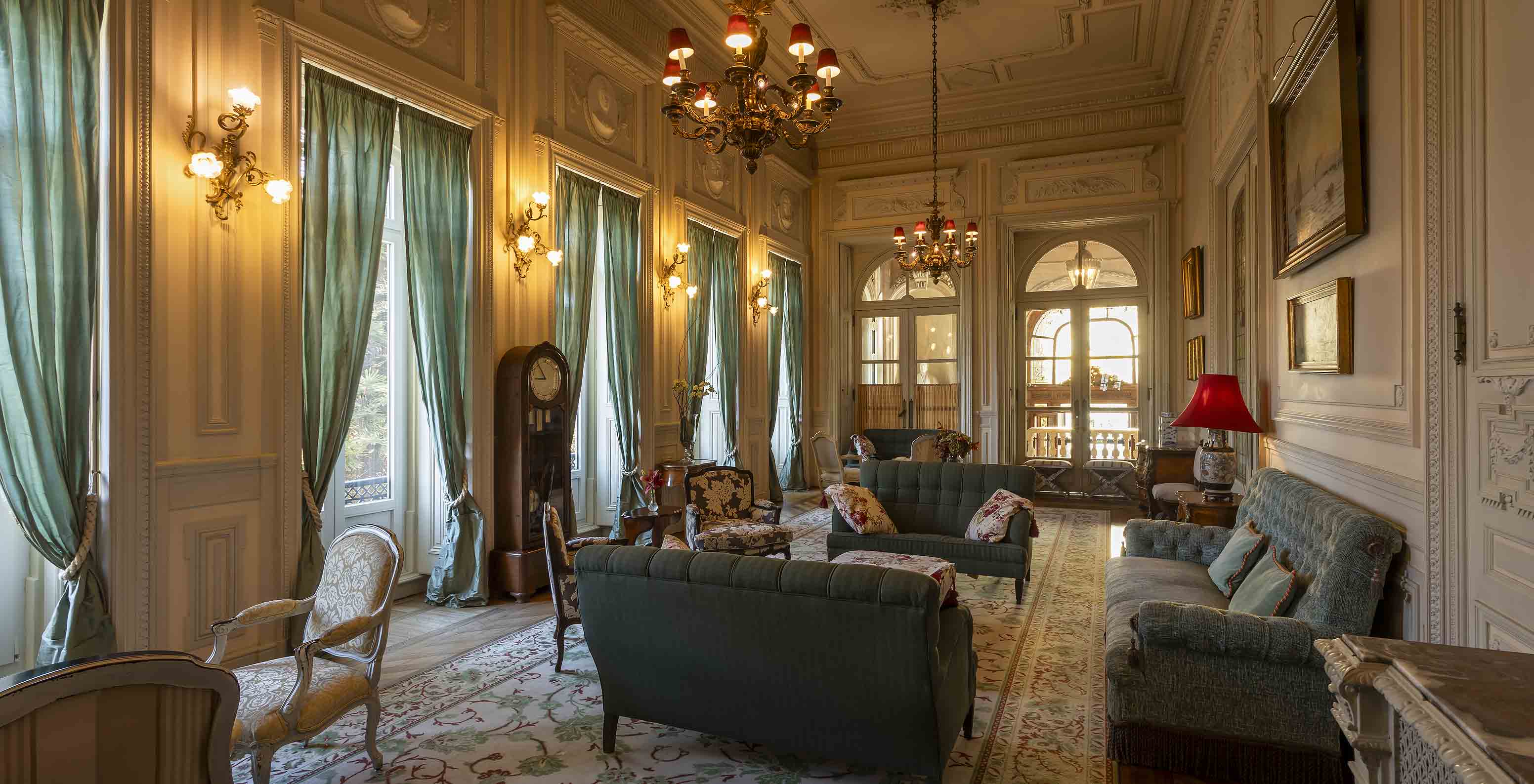 O Pestana Palace Lisboa tem uma sala de estar no palácio com sofás e cadeirões e janelas com longos cortinados verdes
