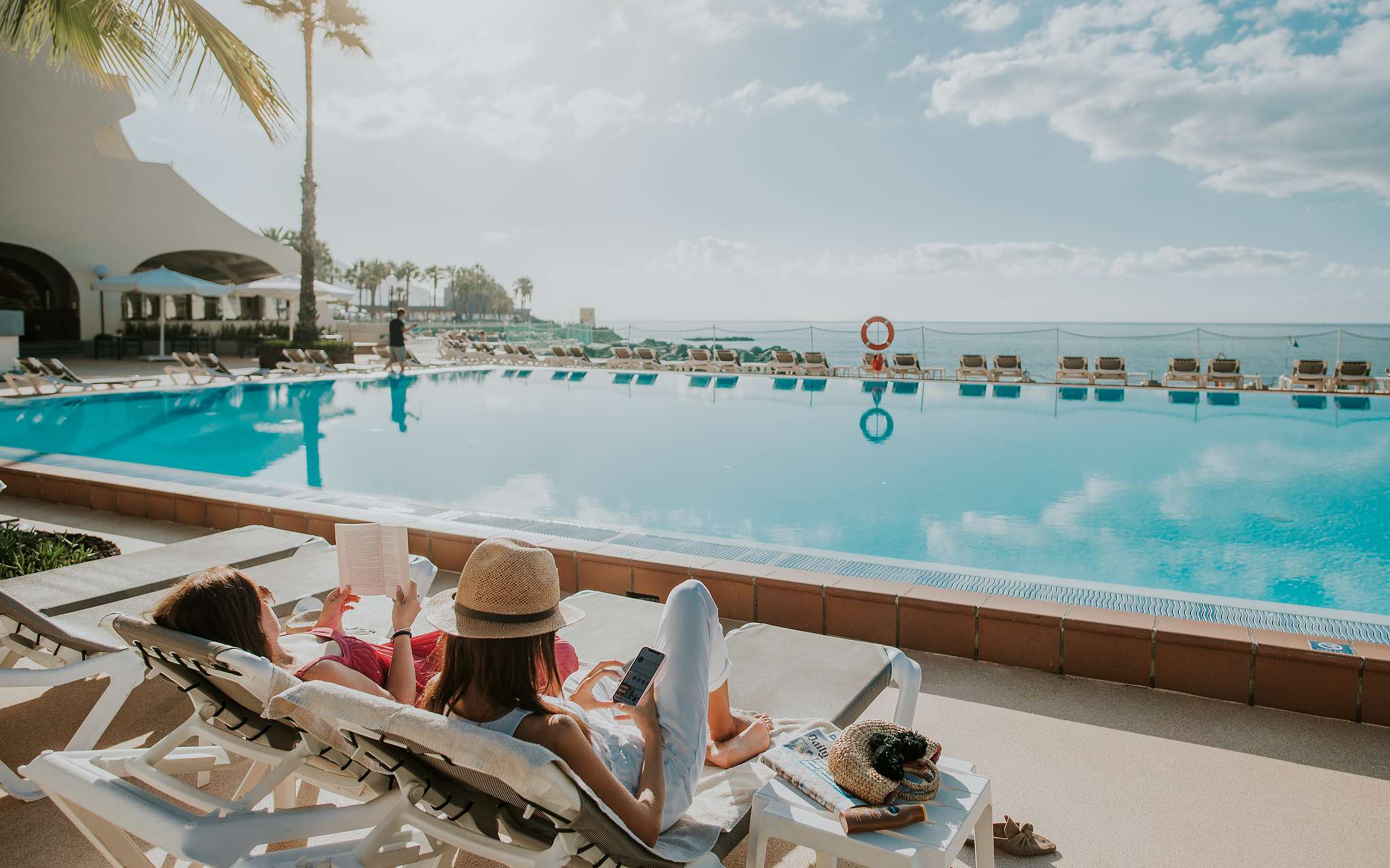 Piscina do Pestana Madeira Beach Club, com vista para o oceano e com duas senhoras deitadas nas espreguiçadeiras a relaxar