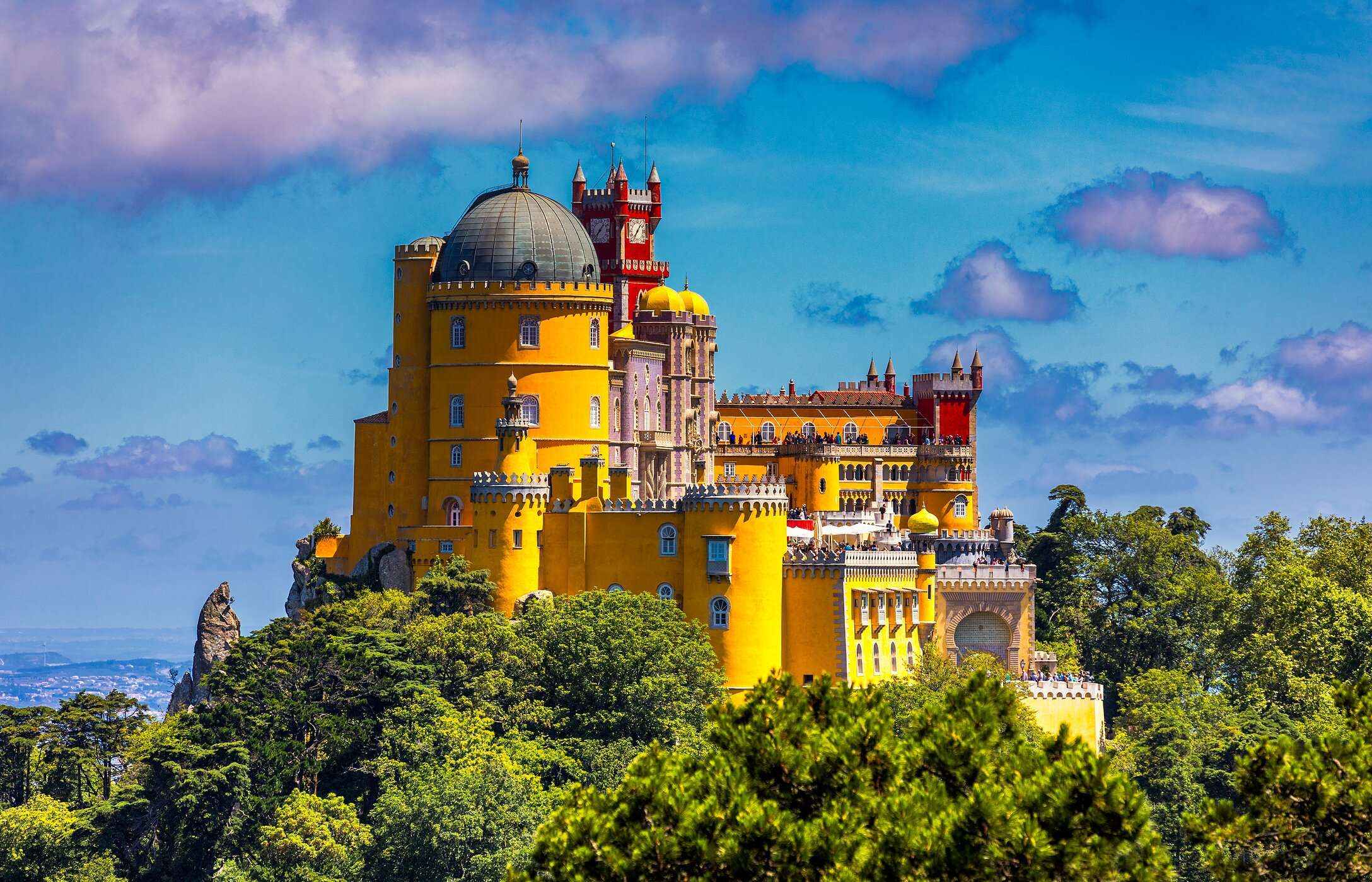 Vista aérea para o Palácio da Pena, em Sintra, com as suas cores vivas, rodeado por vegetação sob um céu azul