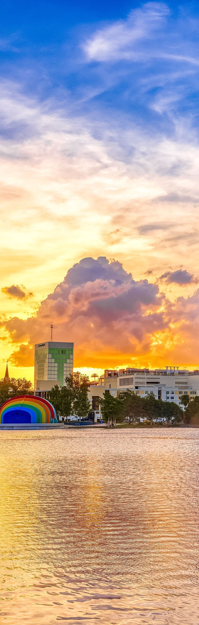 Explore Hotéis em Orlando e desfrute da vista do lago com edifícios e céu colorido ao pôr do sol