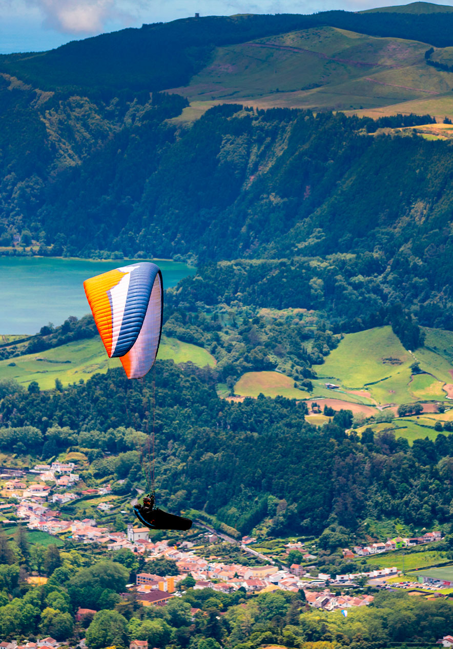 Man paragliden op São Miguel, boven een land met huizen en groene, bergachtige velden