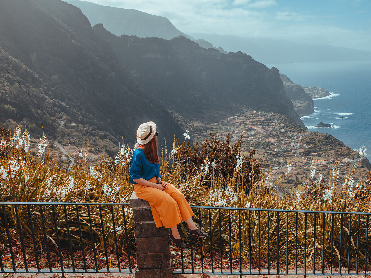 Vrouw zittend op een muur geniet van het uitzicht op een fajã op Madeira, omringd door de zee