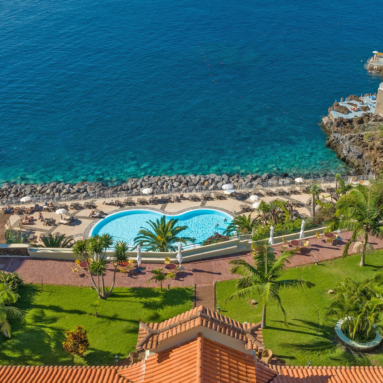 Luchtfoto van Pestana Vila Lido Madeira, met uitzicht op zee, palmbomen eromheen en een zwembad
