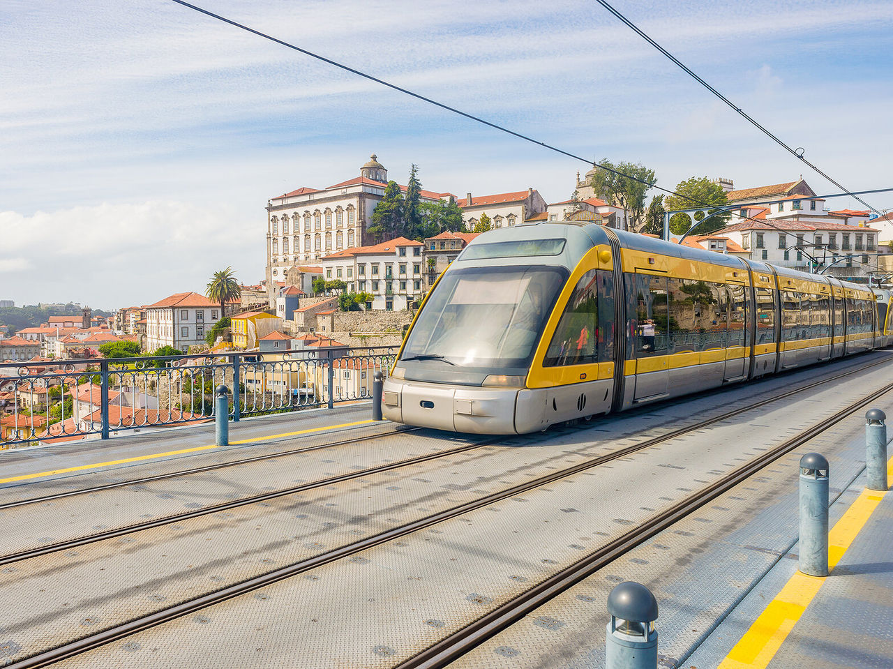 Uitzicht op een moderne gele tram met de historische stad Porto op de achtergrond, met hoge en kleurrijke gebouwen