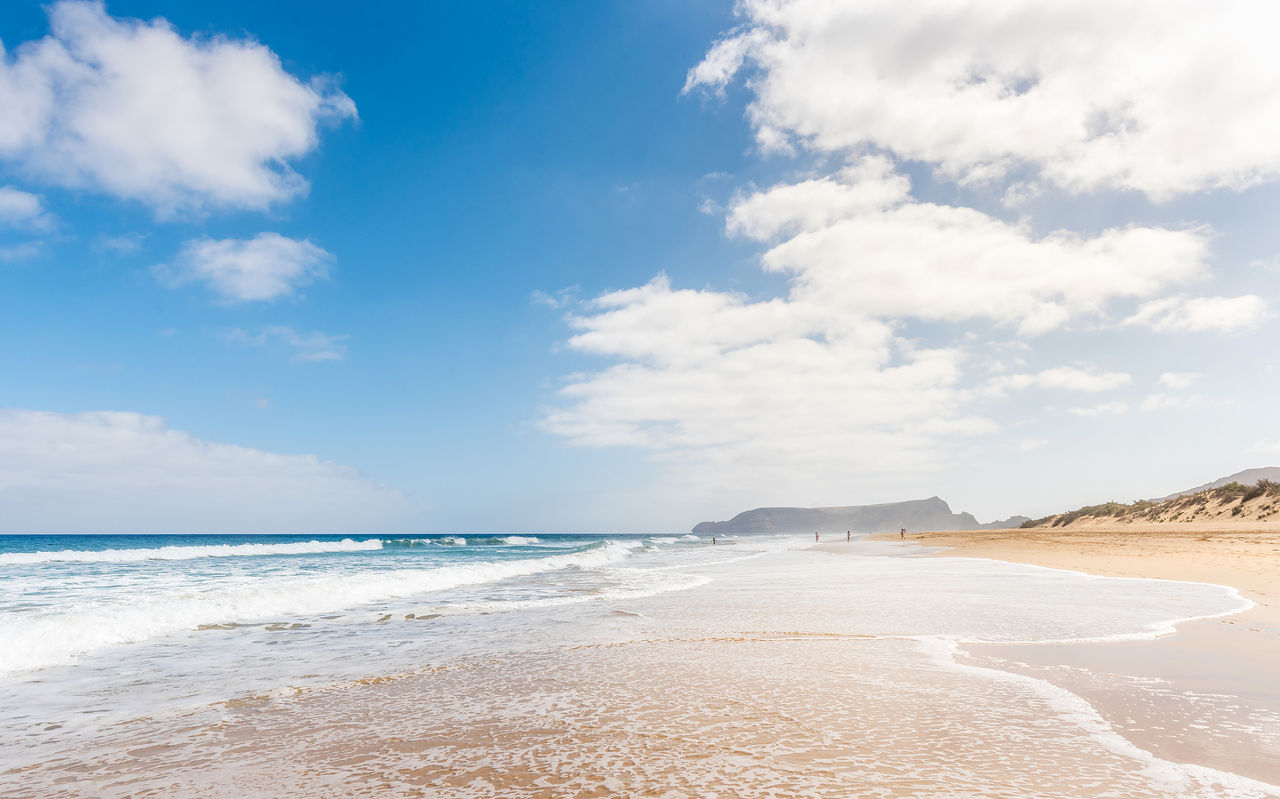 Lang strand in Porto Santo met licht zand, rustige golven en een blauwe lucht met enkele wolken