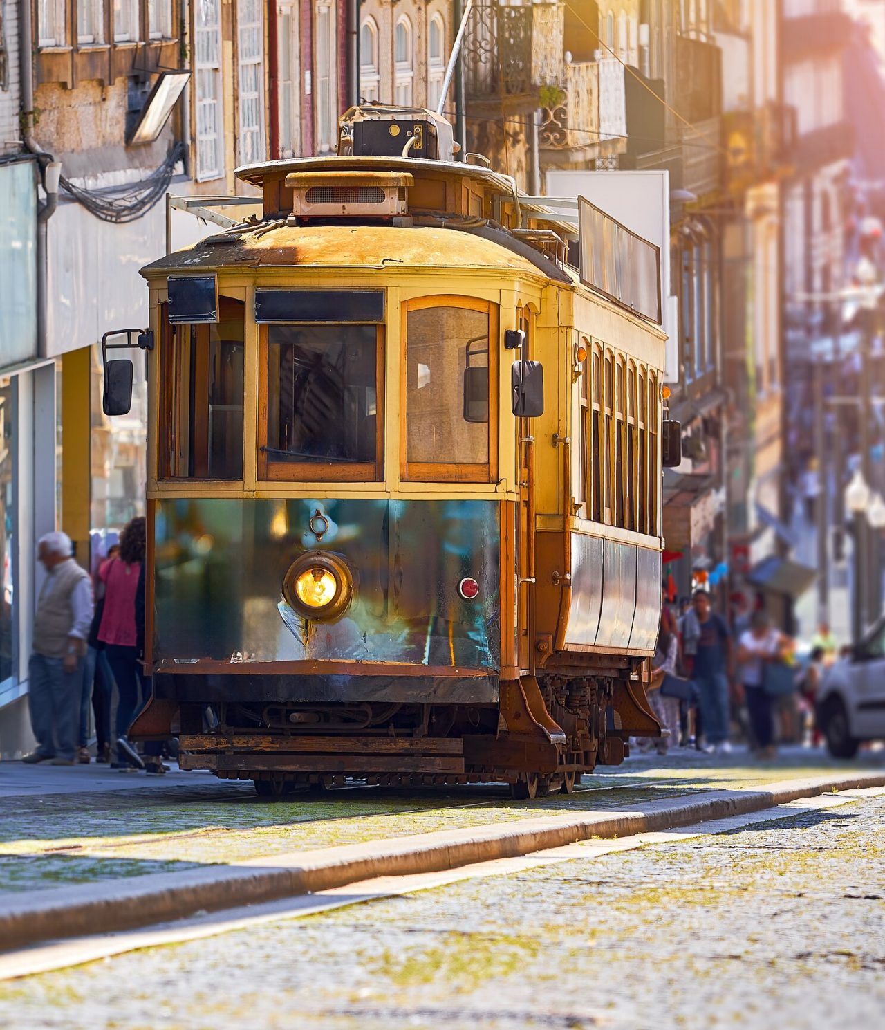 Uitzicht op een oude gele tram die een straat in Porto beklimt, met meerdere mensen achter en oude gebouwen