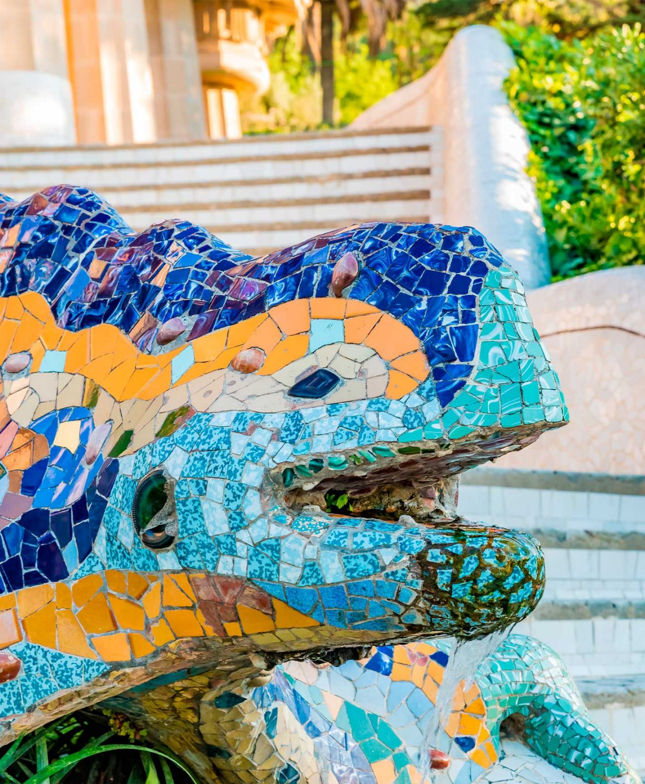 Kleurrijk drakenbeeld, werk van Gaudí, in Park Güell, Barcelona, met trappen en vegetatie op de achtergrond