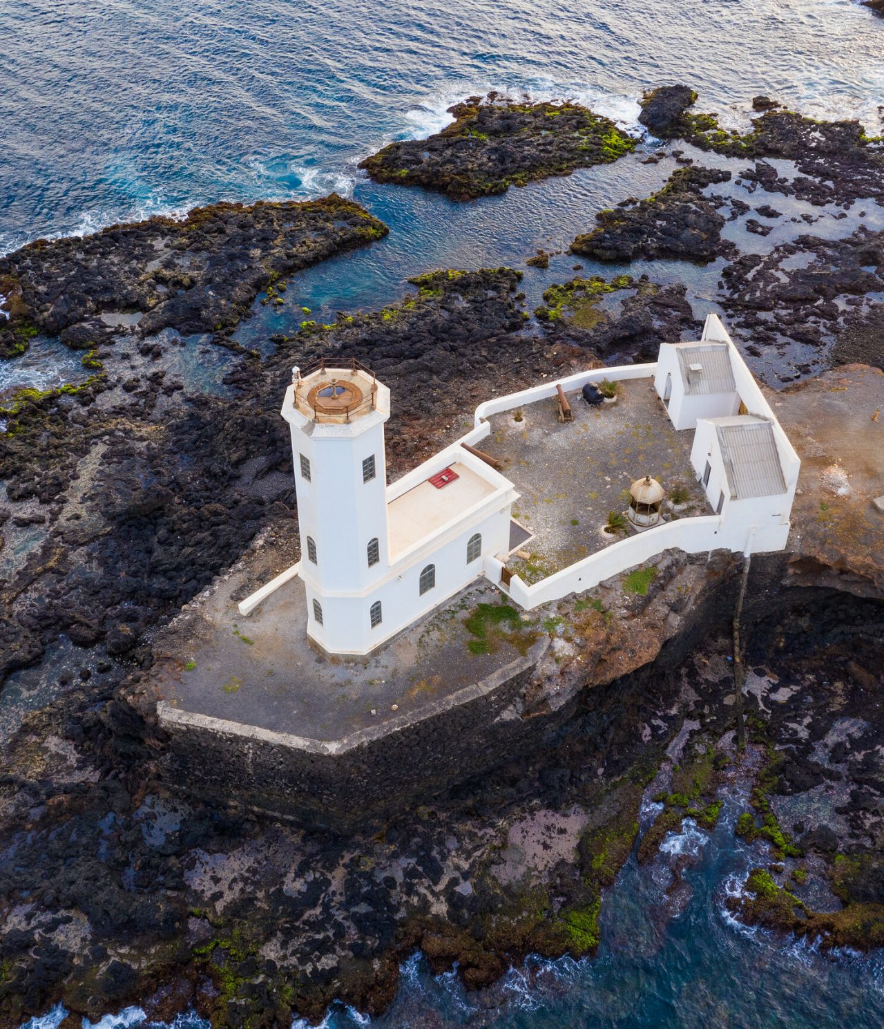 Aerial view of a lighthouse surrounded by the sea and naturally sculpted rocks