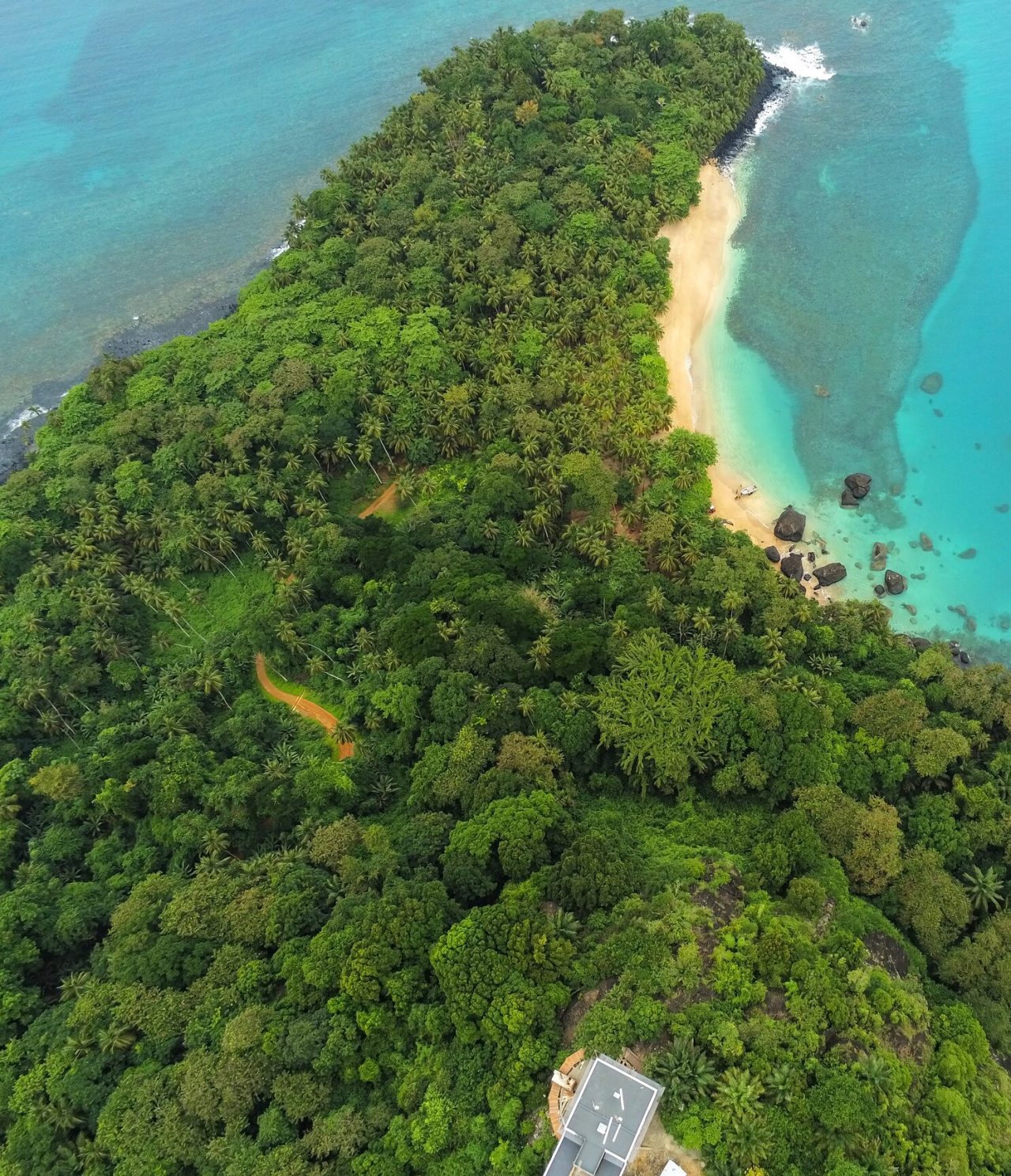 Aerial view of the island of São Tomé and Príncipe, with abundant vegetation, a white sandy beach, and crystal-clear waters