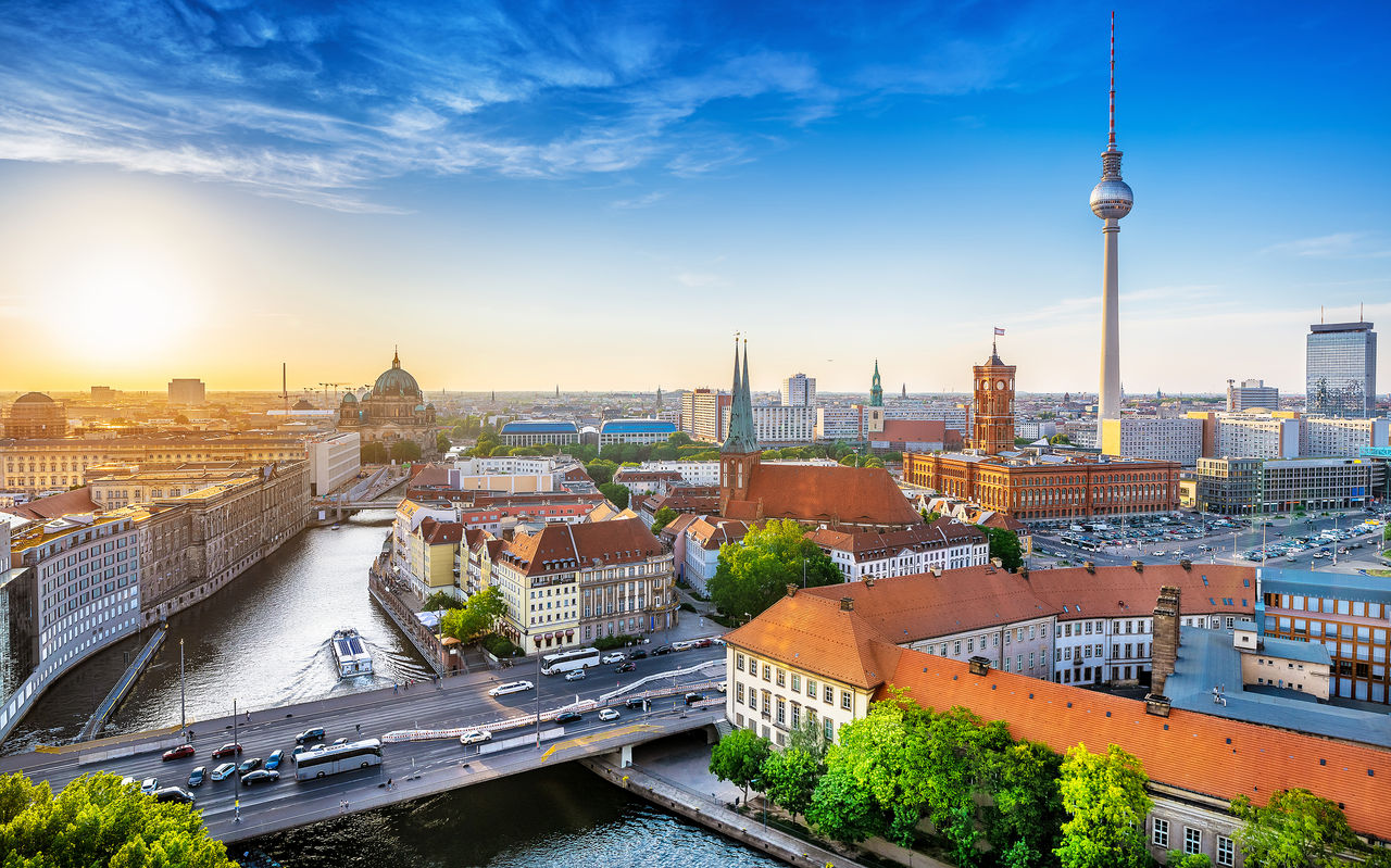 Aerial view over the city of Berlin, with a bridge with cars passing, several buildings, and the iconic television tower