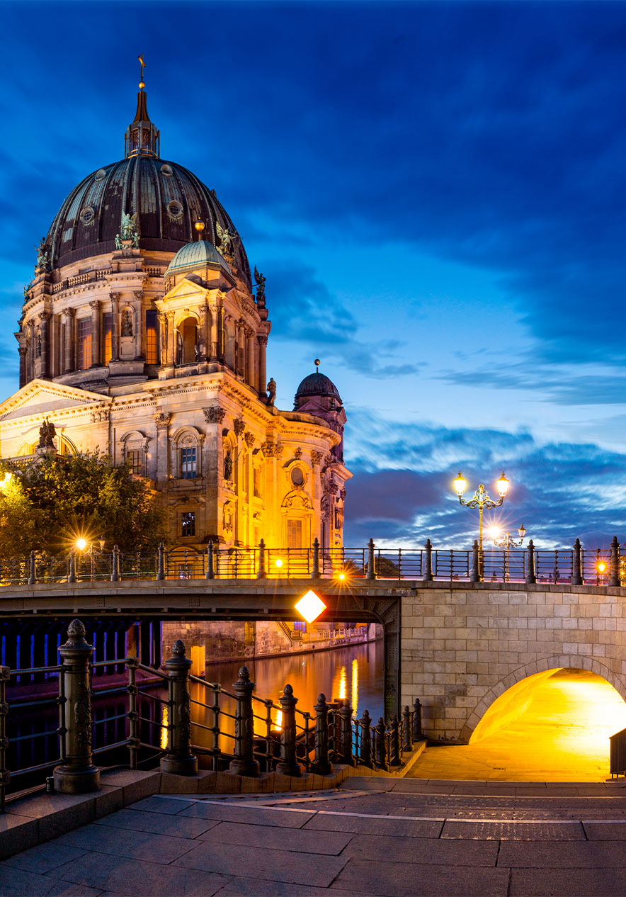 Berlin Cathedral illuminated at dusk with a bridge and modern buildings nearby reflected in the river below