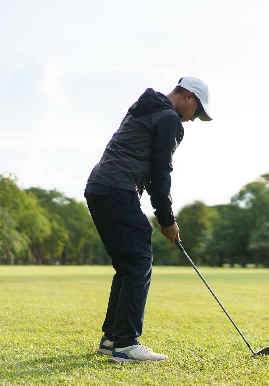 Man in a white hat and sports clothes playing golf on a very green course with blurred trees in the background