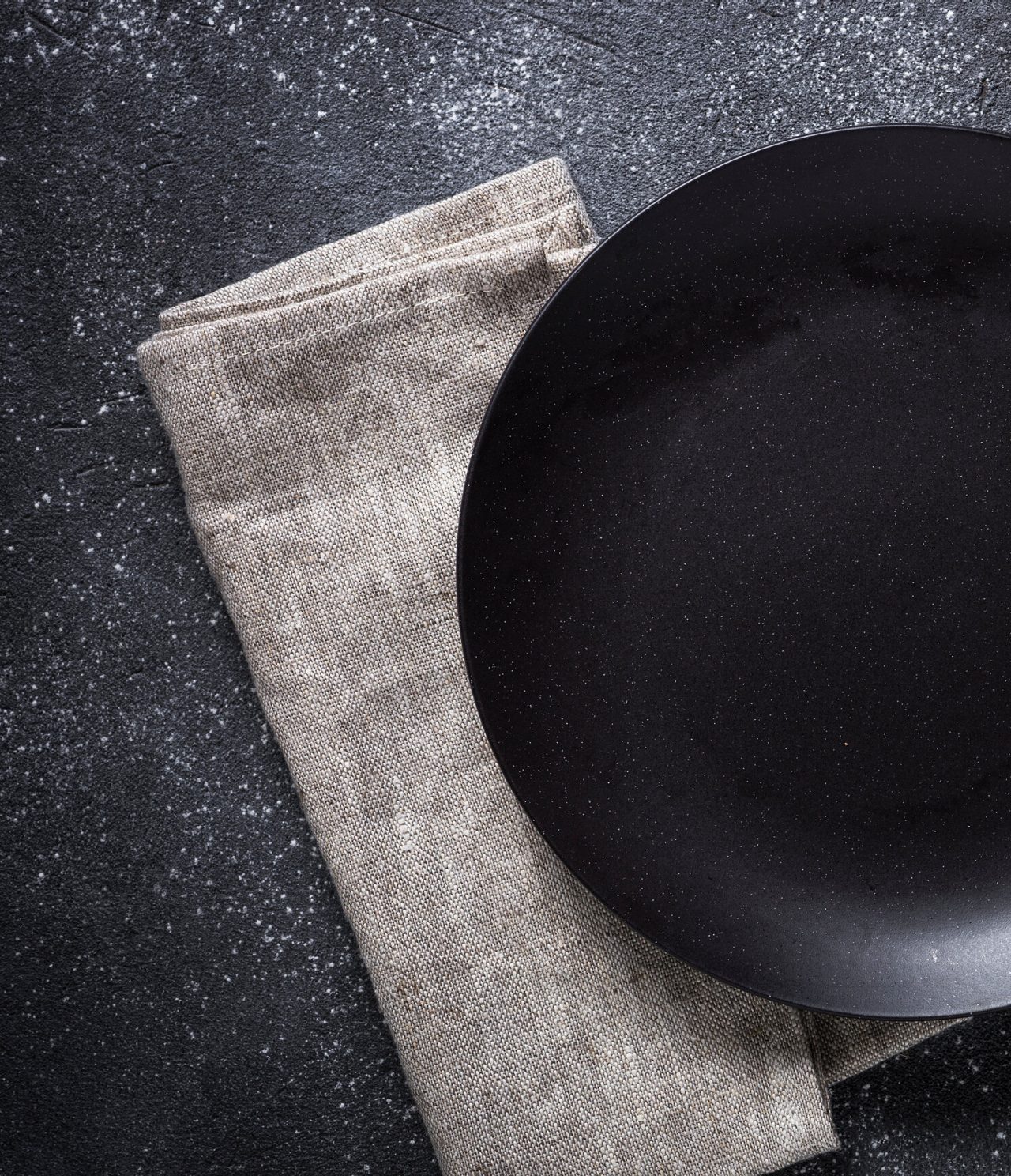 Gourmet dinner plate, matte black, placed on a light gray napkin, on a dark background
