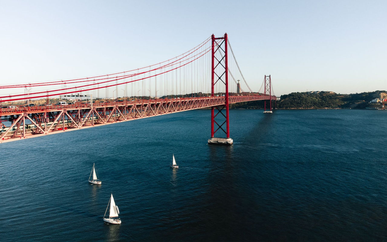 Panoramic view of the city of Lisbon, with the Tejo River featuring several boats and the 25 de Abril Bridge