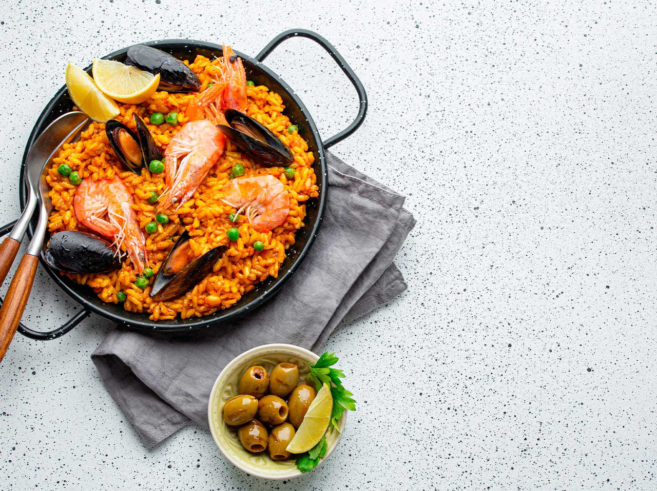 Traditional Spanish dish, a pan of paella, prepared with mussels, shrimp, peas, and rice, served with olives