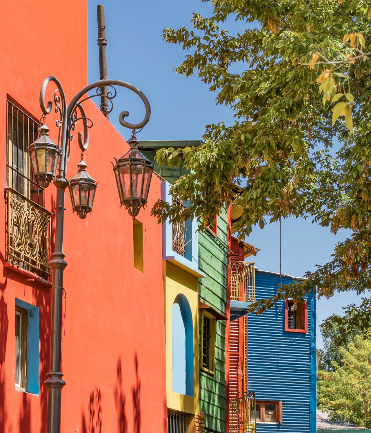 Colorful buildings in the typical Caminito neighborhood in Buenos Aires, with trees in front and a blue sky behind